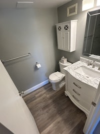 a bathroom with white cabinets and wood floors