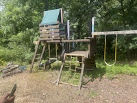 a wooden swing set in a wooded area