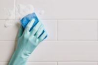 a hand is cleaning a tiled wall with a blue sponge